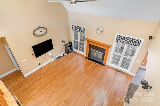 unfurnished living room featuring ceiling fan, light wood-style flooring, baseboards, a tile fireplace, and visible vents