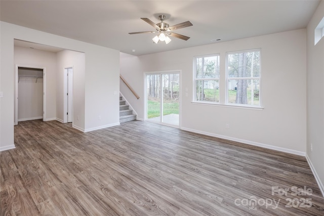 unfurnished living room with baseboards, wood finished floors, ceiling fan, and stairway