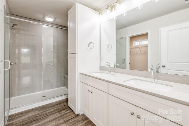 full bath with wood finished floors, a sink, double vanity, and a shower stall