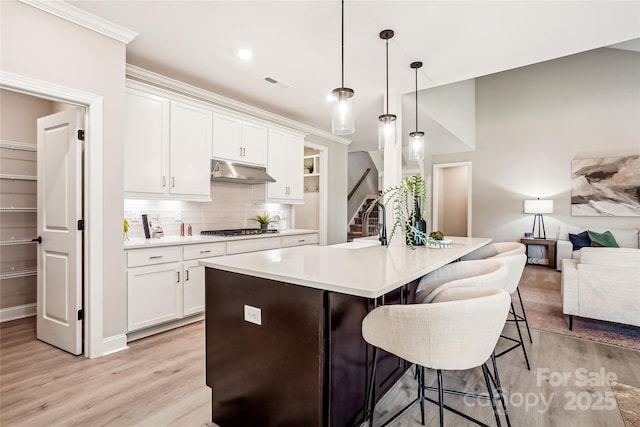 522 Fern Hill Rd Unit 17, Mooresville, NC 28117 - kitchen with under cabinet range hood, light wood-style floors, stainless steel gas cooktop, a kitchen bar, and decorative backsplash