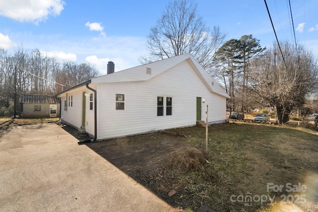 view of side of home featuring driveway, a chimney, and a yard