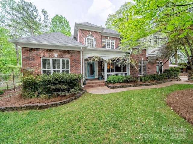 traditional-style home with brick siding, roof with shingles, a porch, and a front yard