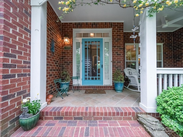 view of exterior entry with brick siding, a ceiling fan, and covered porch