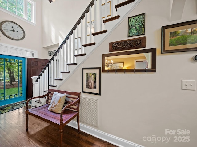 stairway with visible vents, baseboards, wood finished floors, and a towering ceiling