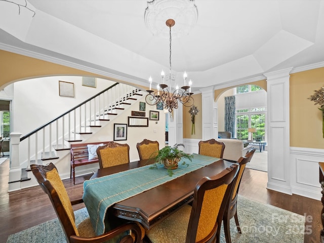 dining area featuring a tray ceiling, arched walkways, decorative columns, stairway, and a decorative wall