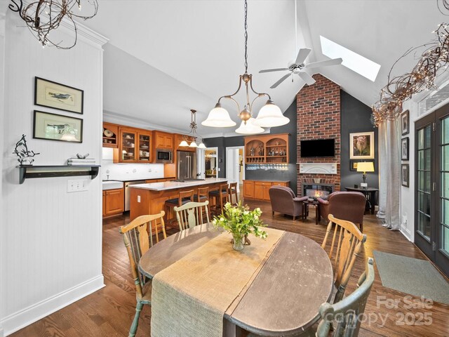 dining space featuring ceiling fan with notable chandelier, a skylight, a fireplace, and dark wood-type flooring