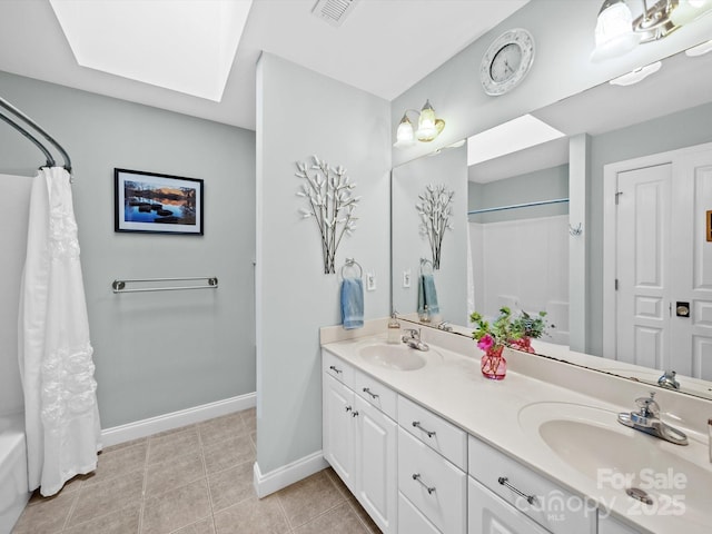 bathroom with double vanity, a skylight, baseboards, and a sink