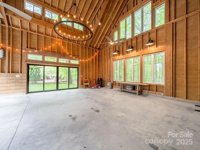misc room with plenty of natural light, concrete flooring, high vaulted ceiling, and a notable chandelier