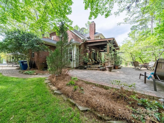 rear view of property featuring a yard, brick siding, and a patio area