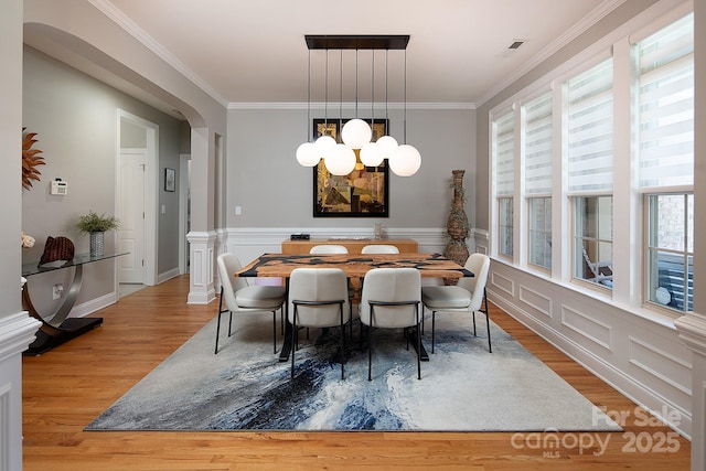 dining area featuring a wainscoted wall, crown molding, wood finished floors, arched walkways, and an inviting chandelier