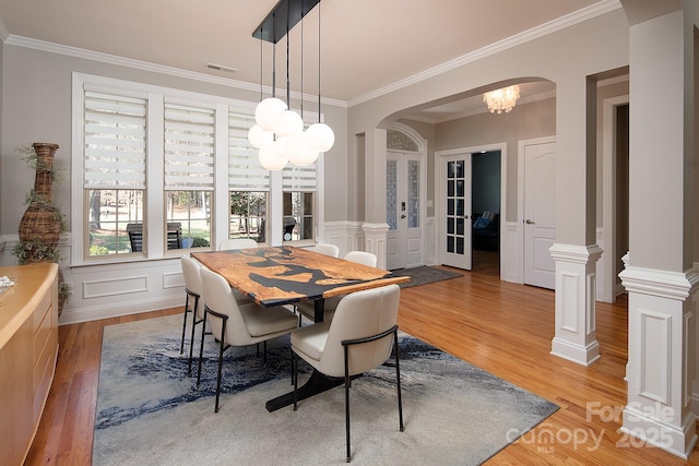 dining space with crown molding, arched walkways, a decorative wall, and light wood-style floors