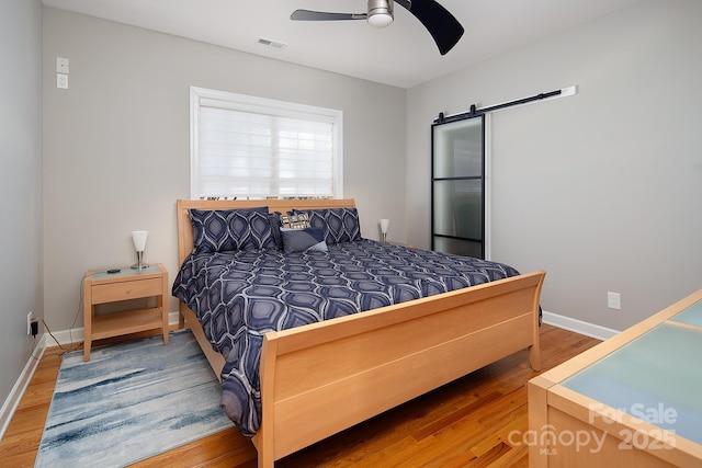 bedroom featuring baseboards, a barn door, ceiling fan, visible vents, and wood finished floors