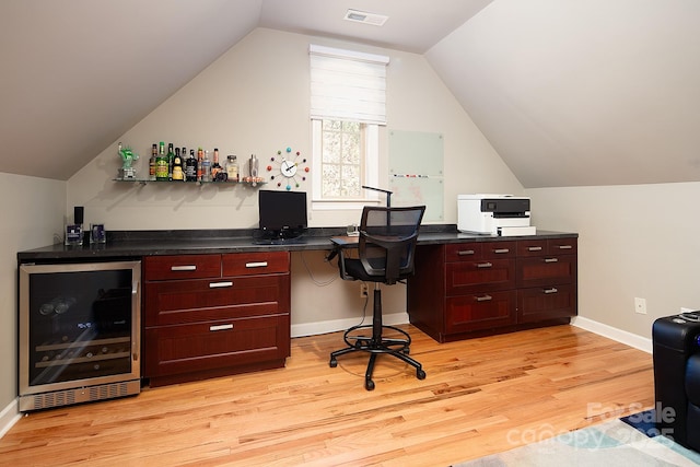 home office featuring lofted ceiling, light wood-type flooring, beverage cooler, visible vents, and a bar