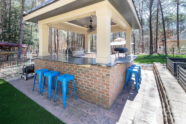 view of patio featuring exterior kitchen, fence, area for grilling, ceiling fan, and outdoor wet bar