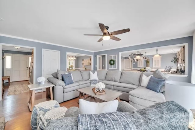 living area with ornamental molding, wood finished floors, and ceiling fan with notable chandelier