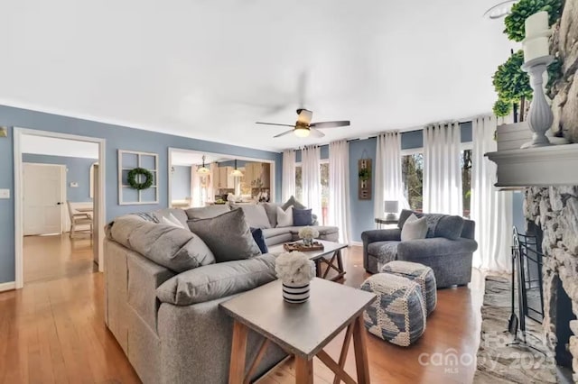 living room with ceiling fan, wood finished floors, and a stone fireplace