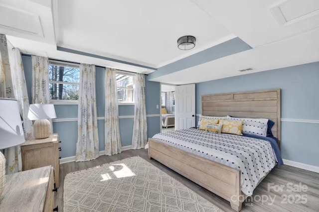 bedroom featuring wood finished floors, attic access, baseboards, and visible vents