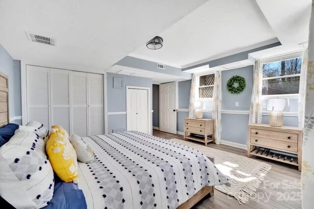 bedroom featuring two closets, baseboards, visible vents, and wood finished floors