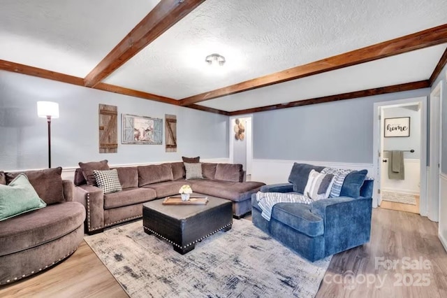 living room featuring wainscoting, wood finished floors, beam ceiling, and a textured ceiling