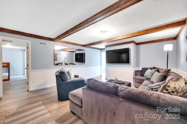 living area with light wood finished floors, beamed ceiling, visible vents, and wainscoting