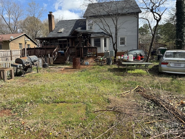 rear view of house featuring a deck, fence, a lawn, and a chimney