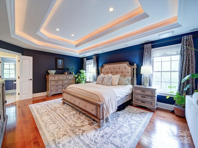 bedroom featuring baseboards, ornamental molding, a tray ceiling, and hardwood / wood-style floors
