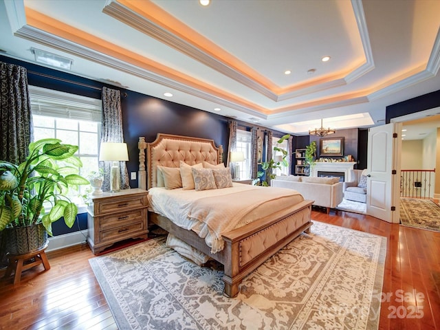 bedroom featuring a raised ceiling, a fireplace, a chandelier, ornamental molding, and hardwood / wood-style flooring