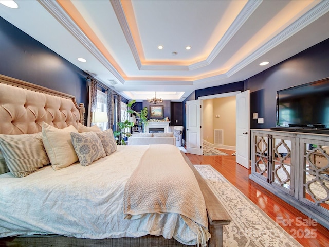 bedroom with crown molding, an inviting chandelier, recessed lighting, wood finished floors, and a tray ceiling