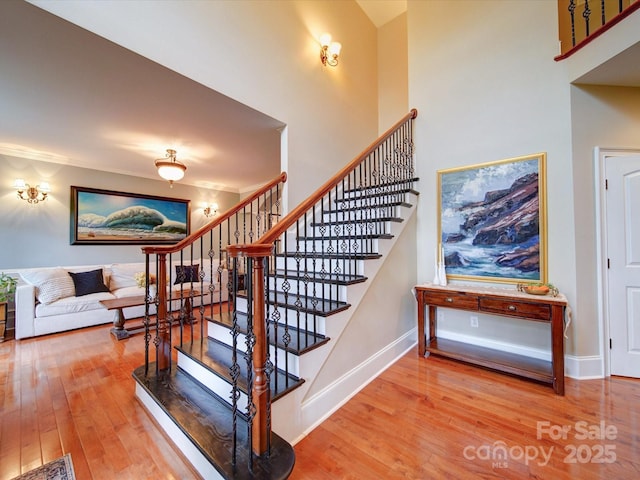 stairway featuring wood-type flooring, baseboards, and a towering ceiling