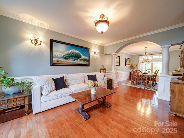 living room with ornate columns, arched walkways, wood finished floors, and ornamental molding