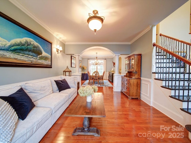 living area featuring decorative columns, crown molding, arched walkways, wood finished floors, and stairway