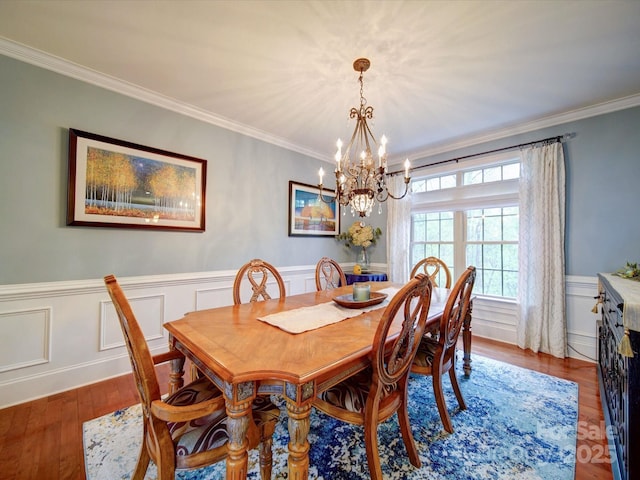 dining room with an inviting chandelier, crown molding, a wainscoted wall, and wood finished floors
