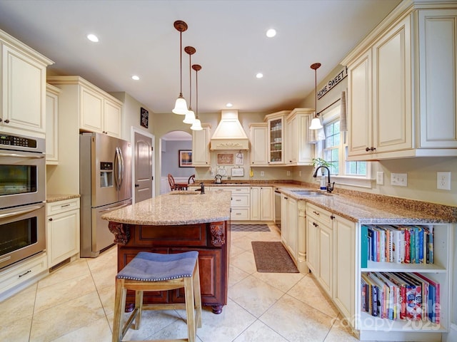 kitchen featuring appliances with stainless steel finishes, arched walkways, light stone counters, and cream cabinetry