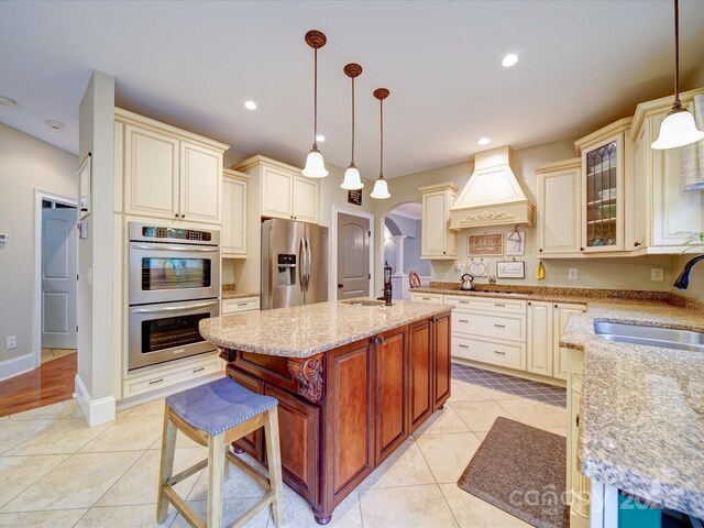 kitchen featuring appliances with stainless steel finishes, a sink, arched walkways, cream cabinetry, and custom range hood
