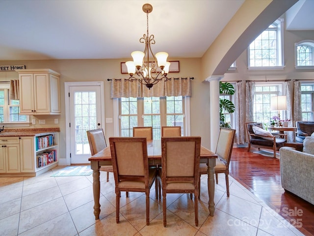 dining area with an inviting chandelier, arched walkways, ornate columns, and light tile patterned flooring