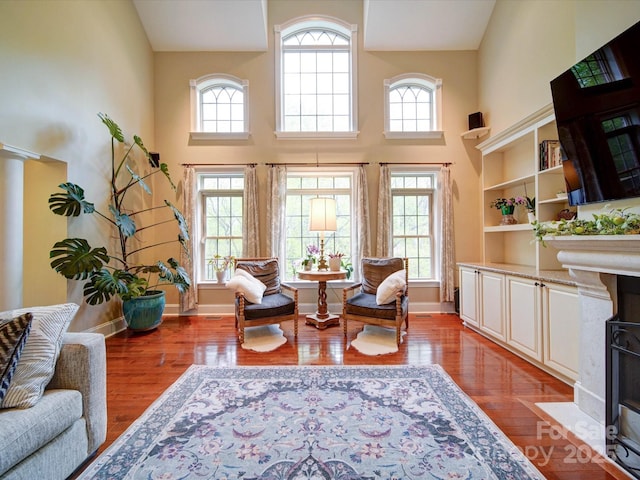 sitting room with a healthy amount of sunlight, wood finished floors, and a towering ceiling