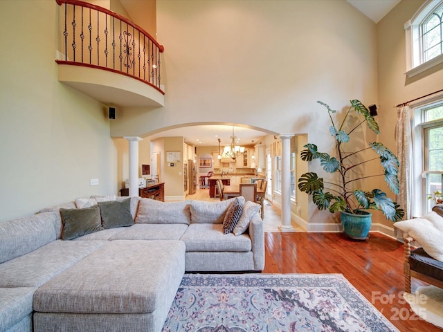 living area with a towering ceiling, wood finished floors, baseboards, ornate columns, and arched walkways
