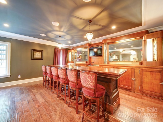 bar featuring crown molding, wet bar, decorative light fixtures, and light wood-style flooring
