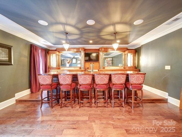 bar featuring a raised ceiling, ornamental molding, and light wood-style flooring