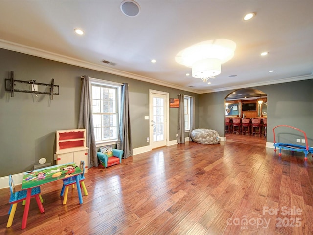 playroom with crown molding, arched walkways, wood finished floors, and visible vents