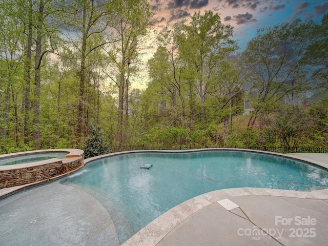 pool at dusk with a pool with connected hot tub