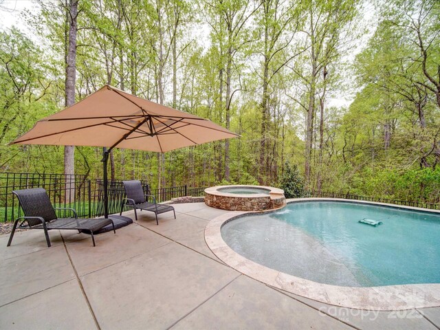 view of swimming pool featuring a patio, a pool with connected hot tub, fence, and a forest view