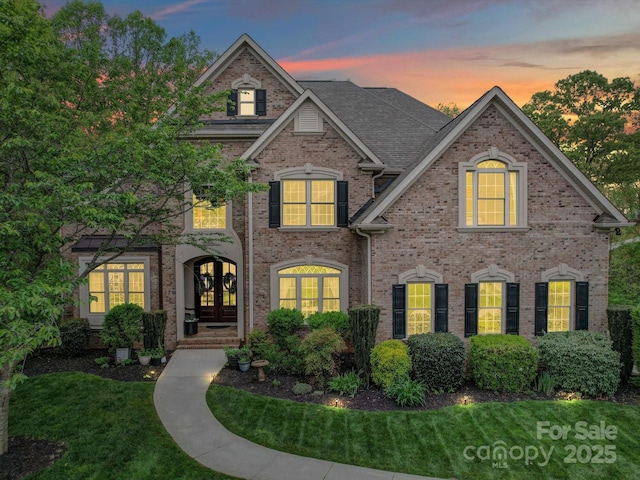 view of front facade featuring a yard, brick siding, and french doors
