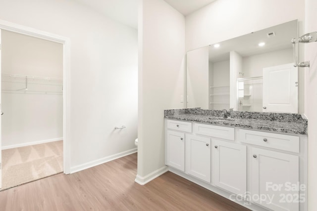 bathroom with vanity, wood finished floors, baseboards, a shower stall, and a spacious closet