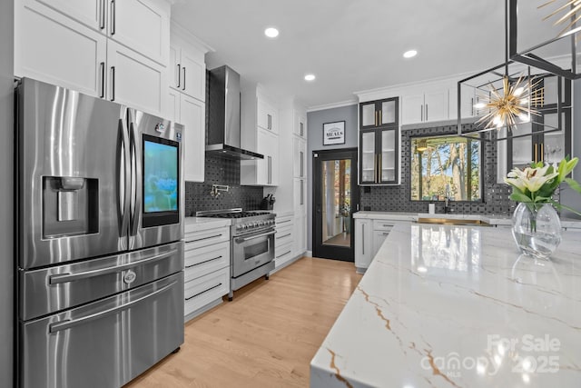 15921 Cramur Dr, Huntersville, NC 28078 - kitchen featuring light wood finished floors, wall chimney exhaust hood, stainless steel appliances, glass insert cabinets, and an inviting chandelier