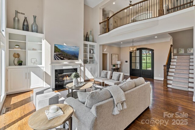 living area with stairs, ornamental molding, baseboards, a glass covered fireplace, and wood finished floors