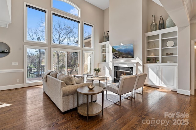 living room featuring dark wood finished floors, baseboards, a high ceiling, and a high end fireplace