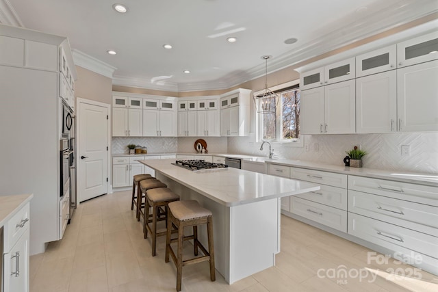 kitchen featuring ornamental molding, a kitchen bar, stainless steel appliances, white cabinetry, and a center island