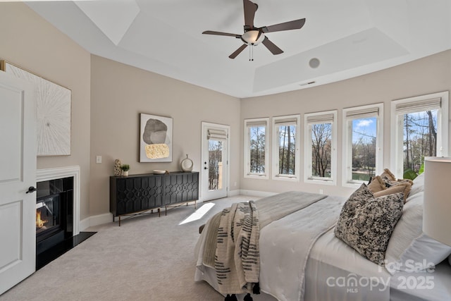 carpeted bedroom featuring visible vents, baseboards, access to outside, a tray ceiling, and a glass covered fireplace