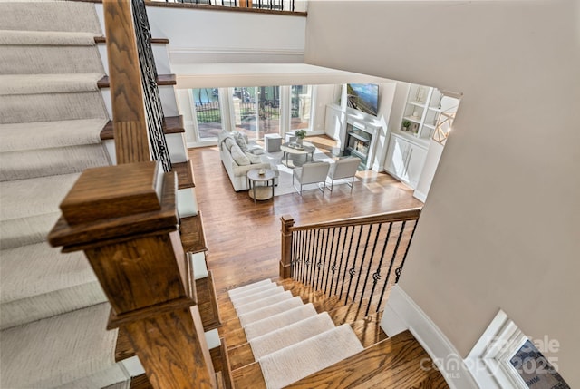 stairs with a warm lit fireplace, baseboards, and wood finished floors